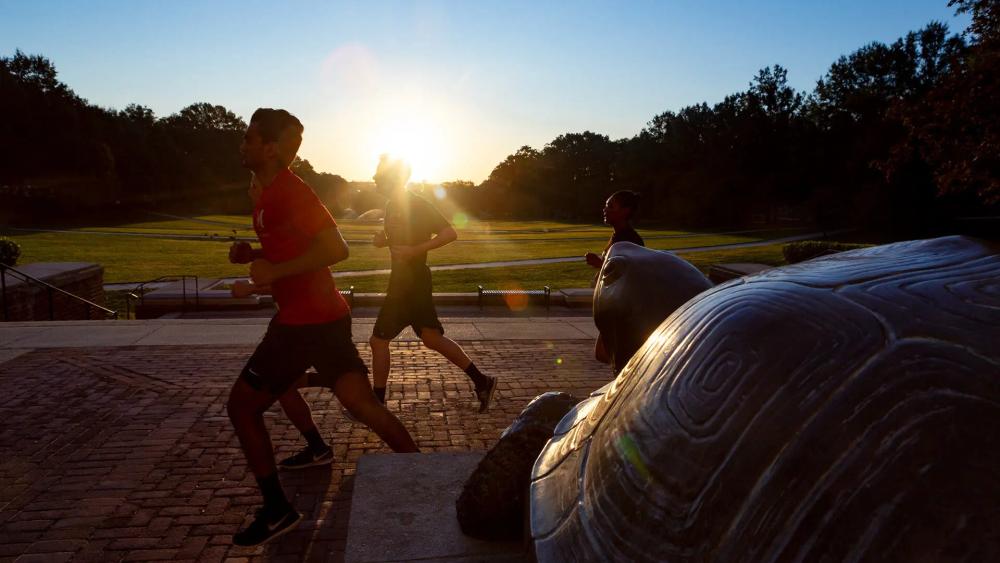 cadets run past testudo statue on mall at sunrise